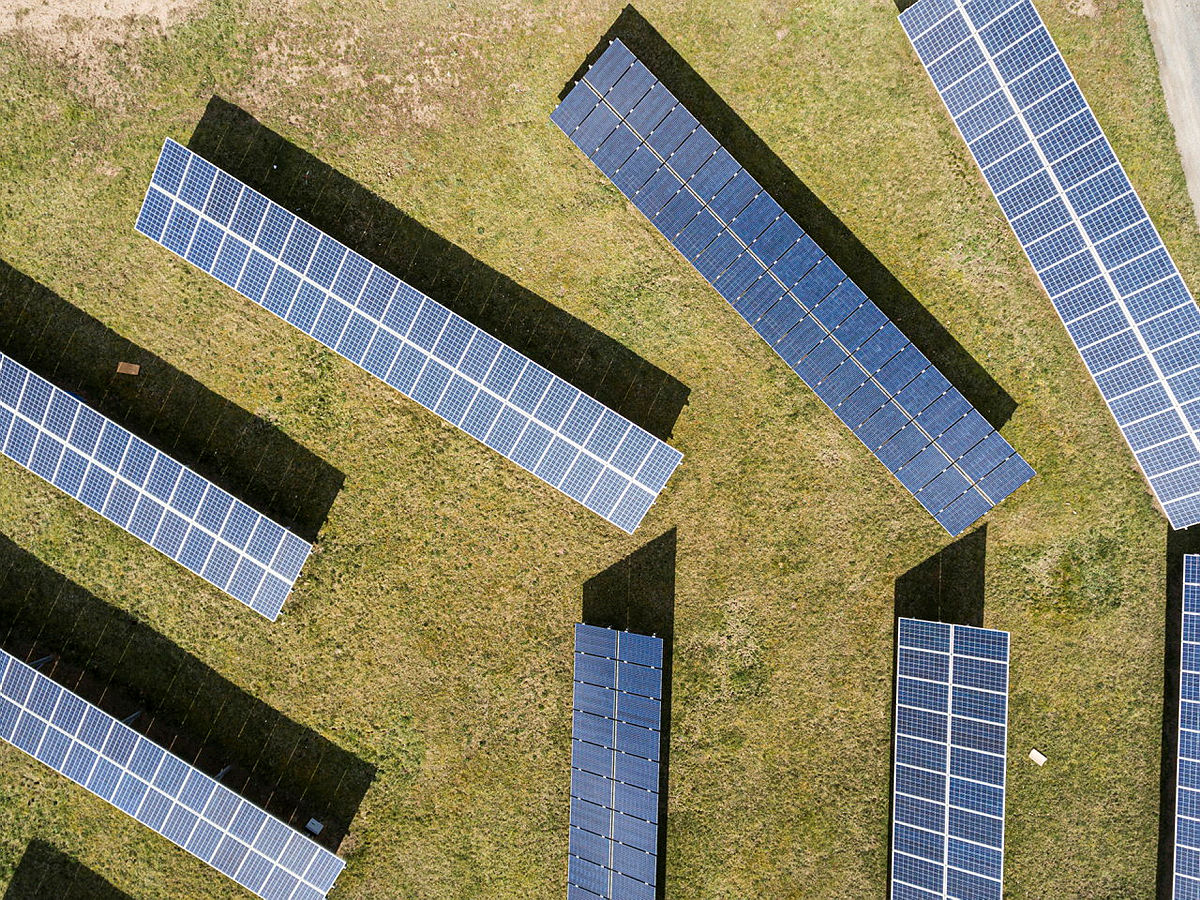 Luftaufnahme von Solarpanelen auf einer grünen Wiese in sonnigem Wetter.